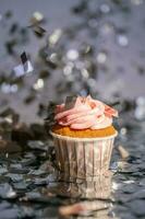 ein Cupcake mit ein Rosa Deckel steht unter das fliegend Silber Konfetti. foto
