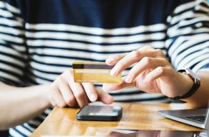Bezahlen Sie online mit der Hand, die eine Kreditkarte hält und mit einem Smartphone foto