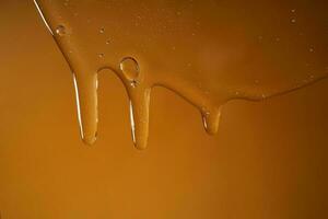 ein fallen von Körper Gel oder Shampoo fließend Nieder auf ein Gelb gesättigt Hintergrund. Textur. foto