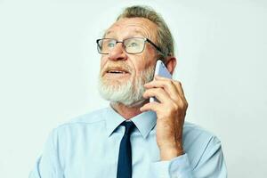 alt Mann im Brille mit ein Telefon im das Studio auf ein Weiß Hintergrund reden foto