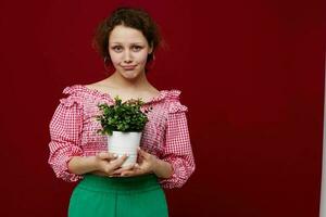 heiter Frau halten ein Topf mit ein Blume im ihr Hände rot Hintergrund foto