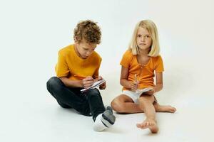 Junge und Mädchen auf das Fußboden mit Notizblöcke und Bleistifte isoliert Hintergrund unverändert foto