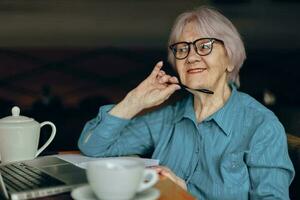 schön reifen Senior Frau Sitzung im ein Cafe mit ein Tasse von Kaffee und ein Laptop Freiberufler funktioniert unverändert foto