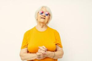 Porträt von ein alt freundlich Frau im beiläufig T-Shirt Sonnenbrille Licht Hintergrund foto