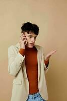 Porträt von ein jung Mann im ein Beige Jacke reden auf das Telefon Licht Hintergrund unverändert foto