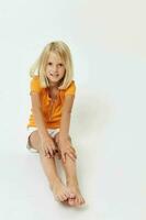 ein heiter wenig Mädchen im ein Gelb T-Shirt sitzt auf das Fußboden mit ihr Beine gefaltet foto