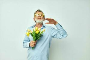 Porträt von glücklich Senior Mann im ein Blau Hemd mit ein Strauß von Blumen Licht Hintergrund foto