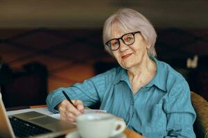 Senior Frau Sitzung im ein Cafe mit ein Tasse von Kaffee und ein Laptop Freiberufler funktioniert unverändert foto