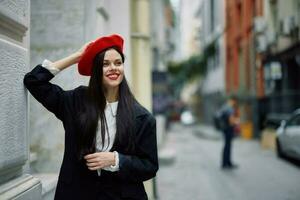 Frau Stehen in der Nähe von ein Mauer im das Stadt tragen ein stilvoll Jacke und rot Baskenmütze mit rot Lippen, Reise und Freizeit, Französisch Stil von Kleid. foto
