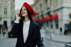 Mode Frau Porträt Lächeln mit Zähne Stehen auf das Straße im das Stadt Hintergrund im stilvoll Kleider rot Lippen und rot Baskenmütze, reisen, filmisch Farbe, retro Jahrgang Stil, städtisch Mode Lebensstil. foto