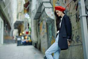 Mode Frau Porträt Gehen Tourist im stilvoll Kleider mit rot Lippen Gehen Nieder ein eng Stadt Straße, reisen, filmisch Farbe, retro Jahrgang Stil, dramatisch gegen ein Mauer mit Graffiti. foto