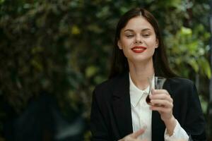 Frau mit rot Lippen Lächeln mit Zähne Getränke Tee im ein Cafe von ein Türkisch Glas Becher im ein Weiß Hemd und schwarz Mode Jacke auf das Straße, Sommer- reisen, Ferien im das Stadt foto