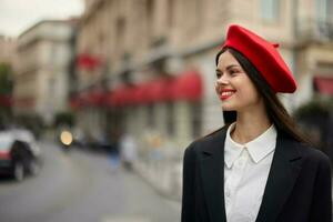 Mode Frau Porträt Lächeln Zähne Stehen auf das Straße im das Stadt Hintergrund im stilvoll Kleider mit rot Lippen und rot Baskenmütze, reisen, filmisch Farbe, retro Jahrgang Stil, städtisch Mode Lebensstil. foto