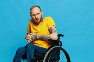 ein Mann sitzt im ein Rollstuhl im ein T-Shirt auf ein Blau Hintergrund im das Studio, das Konzept von ein kostenlos barrierefrei Umgebung zum Menschen mit Behinderungen foto