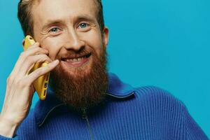 Porträt von ein Mann mit ein Telefon im seine Hände tut suchen beim es und reden auf das Telefon, auf ein Blau Hintergrund. kommunizieren online Sozial Medien, Lebensstil foto