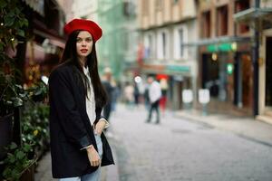 Frau Mode Modell- steht auf das Straße im das Stadt unter das Menge im ein Jacke und rot Baskenmütze und Jeans, filmisch Französisch Mode Stil Kleidung, Reise zu Istanbul foto