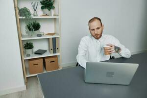 ein Mann im ein Rollstuhl ein Geschäftsmann mit Tätowierungen im das Büro funktioniert beim ein Laptop mit Kaffee, Integration in Gesellschaft, das Konzept von Arbeiten ein Person mit Behinderungen, Freiheit von Sozial Rahmen foto