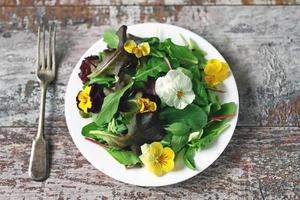 Salatmischung mit Blumen auf einem weißen Teller foto