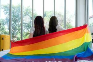 das lgbt Paar saß auf das Bett, bedeckt im Regenbogen Flaggen, spähen aus das Fenster zu beobachten das Natur im das Hotel Zimmer. foto