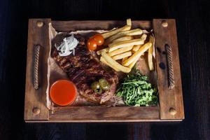 Filetsteak mit Pommes Frites auf einem Holztablett, schöne Portion, dunkler Hintergrund foto