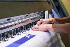 Techniker, der ein Vinylpapier auf einem großen Tintenstrahldrucker fängt foto