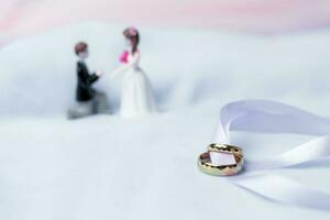 golden Hochzeit Ringe zum Engagement. Ehe golden Ringe mit Weiss, Rosa Bänder Hintergrund. Ringe auf das Weiß und rot Rose. das Ehe Ringe ist das Symbol von traditionell Hochzeit von Paar Liebhaber. foto