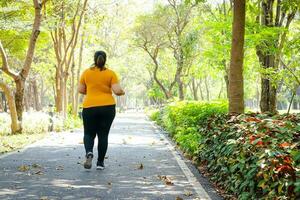 Fett asiatisch Frau tragen Gelb Bluse Joggen im das Morgen im das Park. Konzept von Gewicht Verlust Übung zum das gut Gesundheit von fettleibig Personen. Kopieren Raum foto