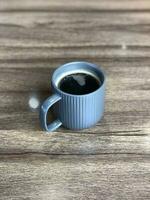 Blau Tasse mit schwarz Kaffee und Holz Korn Tabelle foto