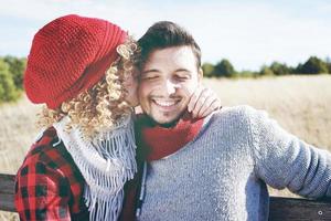 Romantisches junges Paar einer schönen blonden Frau mit lockigem Haar und einer roten Wollmütze, die ihren Freund und einen gutaussehenden Mann im Freien küsst foto