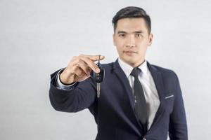 gut aussehender Geschäftsmann mit Autoschlüssel auf grauem Hintergrund foto