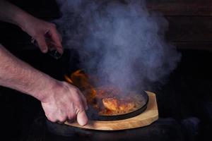Fajitos, Fleisch in einer Pfanne mit Feuer auf einem Holztablett, schöne Portion, dunkler Hintergrund foto