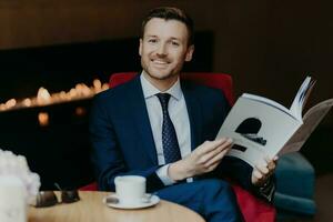 heiter jung Geschäftsmann im Luxus Anzug, lächelt, hält Tagebuch, Getränke Kaffee während Arbeit brechen foto