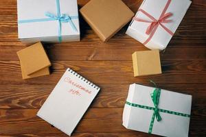 Holztisch mit Geschenkboxen und Notizblock mit Liste der Weihnachtsgeschenke. foto