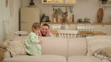 glücklich Familie beim heim. Mutter und Baby Mädchen spielen im Couch beim Zuhause drinnen. wenig Kleinkind Kind und Babysitter Tagesmutter haben Spaß zusammen. jung Frau Mama Kind Tochter sich ausruhen im Leben Zimmer. foto