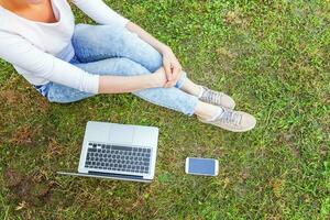 Frauenbeine auf grünem Rasen im Stadtpark, Hände arbeiten am Laptop-PC-Computer. freiberufliches Geschäftskonzept foto