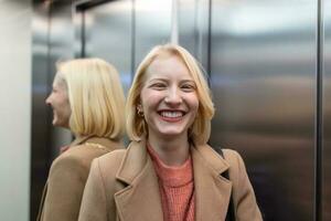 süß blond weiblich im modisch Mantel bleiben im Aufzug allein und lächelnd, Frau im Aufzug foto
