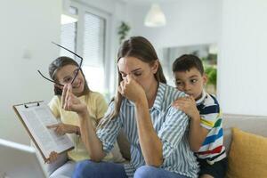 verärgert Mutter haben Problem mit laut frech Tochter und Sohn Springen auf Couch und schreiend, Anspruchsvoll Aufmerksamkeit, frustriert Mama müde von schwierig Kind versuchen zu Arbeit von Zuhause foto