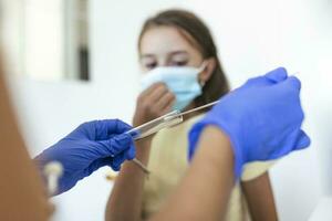 Krankenschwester durchführen ein Mund Tupfer Prüfung auf ein wenig Kind. Mädchen gehen durch pcr testen fällig zu covid-19 Pandemie. weiblich Arzt mit Baumwolle Tupfer während pcr testen klein Mädchen foto