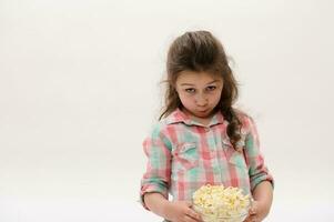 schön Baby Mädchen im stilvoll Rosa und Blau Plaid Shirt, halten Schüssel mit köstlich Popcorn, isoliert auf Weiß Hintergrund foto