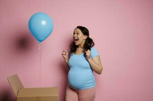 glücklich schwanger Frau Zusammenpressen Fäuste von Aufregung zu Sein Zukunft Mama von ein Junge isoliert auf Rosa Hintergrund. Baby Dusche foto