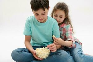 schön Kinder, Teen Junge und wenig Mädchen, Bruder und Schwester Essen Popcorn, haben Spaß zusammen, isoliert Hintergrund. foto