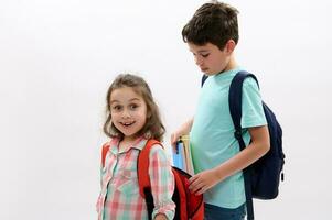 schön Kind Mädchen macht Gesichter suchen beim Kamera während ihr Bruder setzt Arbeitsmappen Innerhalb ihr Rucksack Über Weiß Hintergrund foto