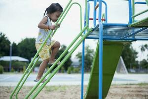 ein Mädchen ist Klettern oben ein Stahl Leiter zu ein rutschen im ein Spielplatz. foto