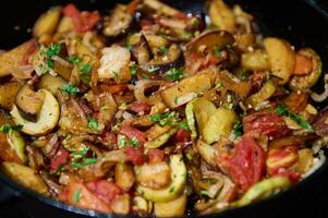 Essen Hintergrund mit Gemüse Eintopf, Ratatouille von geröstet Gemüse bestreut mit frisch Kräuter, im ein Gusseisen Bratpfanne foto