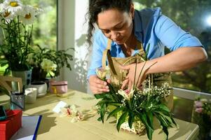 weiblich Florist arrangieren ein Blume Strauß, Einfügen Orchidee Blume in ein eingeweicht Schaum im ein Korbweide Korb im Blumen- Geschäft foto