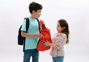 preteen Junge Tragen Orange Rucksack von seine jünger Schwester, bereit zu gehen zum Schule, isoliert Über Weiß Hintergrund. foto