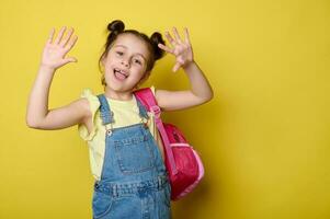 heiter Vorschulkind Mädchen mit Rucksack, zeigt an beim Kamera ihr Hände Palmen, lächelnd genießen das Start von Neu Schule Jahr foto