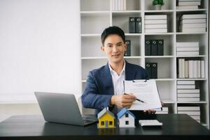 asiatisch Mann Arbeiten mit Haus Modell- echt Nachlass Agent und Kunde diskutieren zum Vertrag zu Kaufen Haus, Versicherung oder Darlehen echt Nachlass konsultieren über Hypothek Darlehen Angebot foto