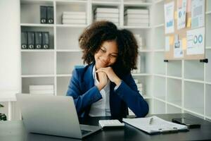 schön afrikanisch Frau Tippen auf Tablette und Laptop während Sitzung beim das Arbeiten hölzern Tabelle modern Büro foto