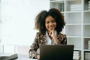 jung schön afrikanisch Frau Tippen auf Tablette und Laptop während Sitzung beim das Arbeiten hölzern Tabelle modern Büro foto